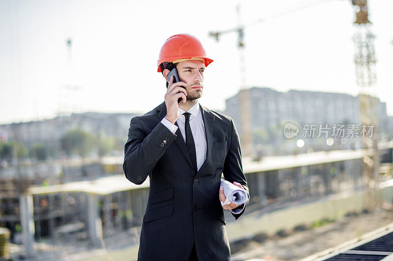 年轻的建筑工程师与项目和安全帽使用电话