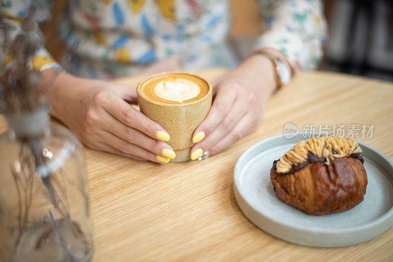 女性手拿着扁平的白咖啡，放在木桌上，旁边是丹麦巧克力