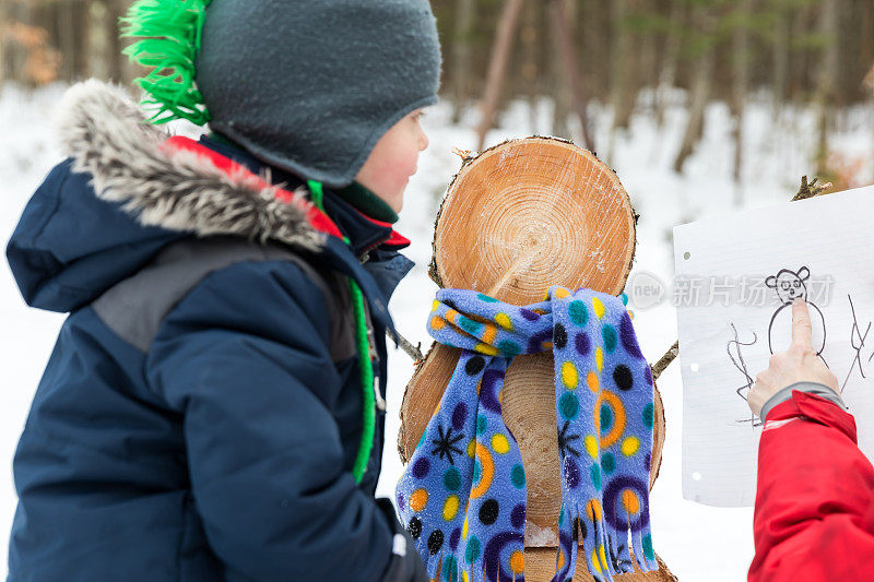 母亲和儿子在冬天户外做一个木制雪人