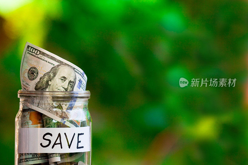 玻璃罐与美元和节省纸标签上模糊的绿色背景。