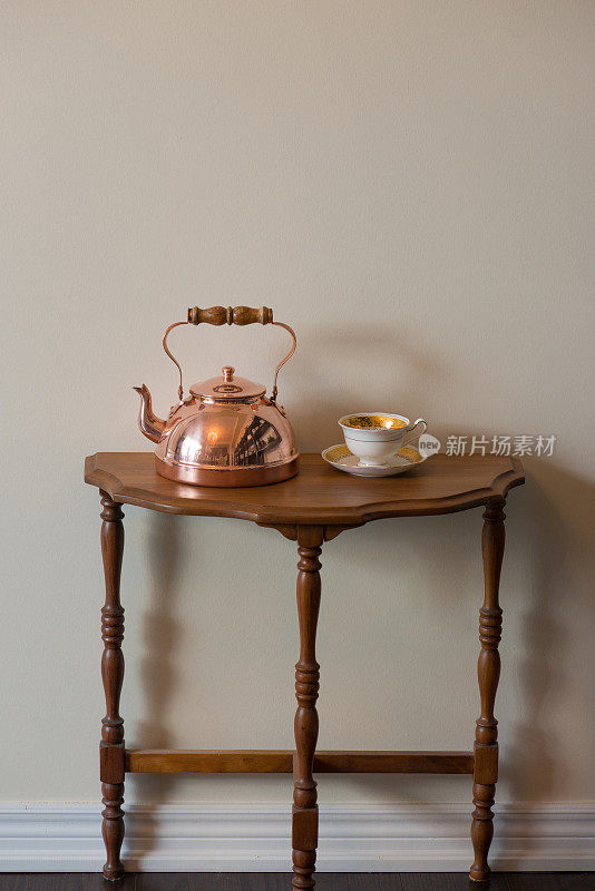 傍晚阳光下胡桃木边桌上的古董铜茶壶和古董英式茶杯