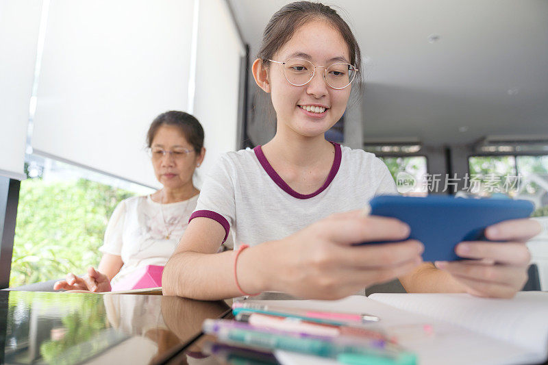 亚洲家庭的青少年和妈妈使用数字平板电脑和智能手机在家里进行电子学习，放松与网上购物使用信用卡和社交网络上的短信电子商务