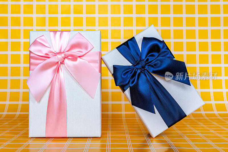 两个白色礼品盒，一个是粉色的，一个是蓝色的，上面有一张黄色格子的背景照片