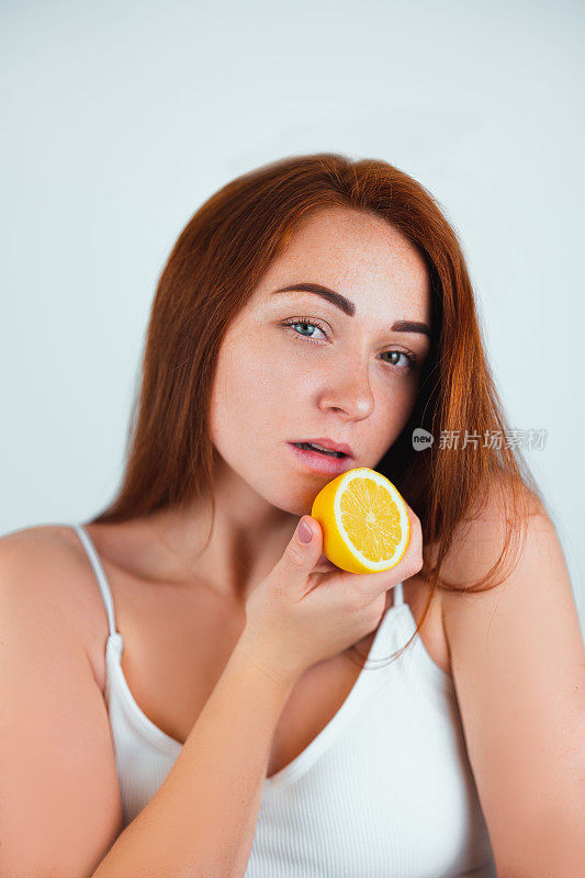 肖像红发年轻女子站在孤立的白色背景拿着一半的橙色在她的脸附近，美丽肖像的概念