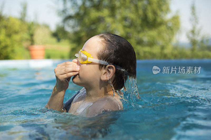 一个小男孩正在后院的游泳池里享受夏天的玩耍时光