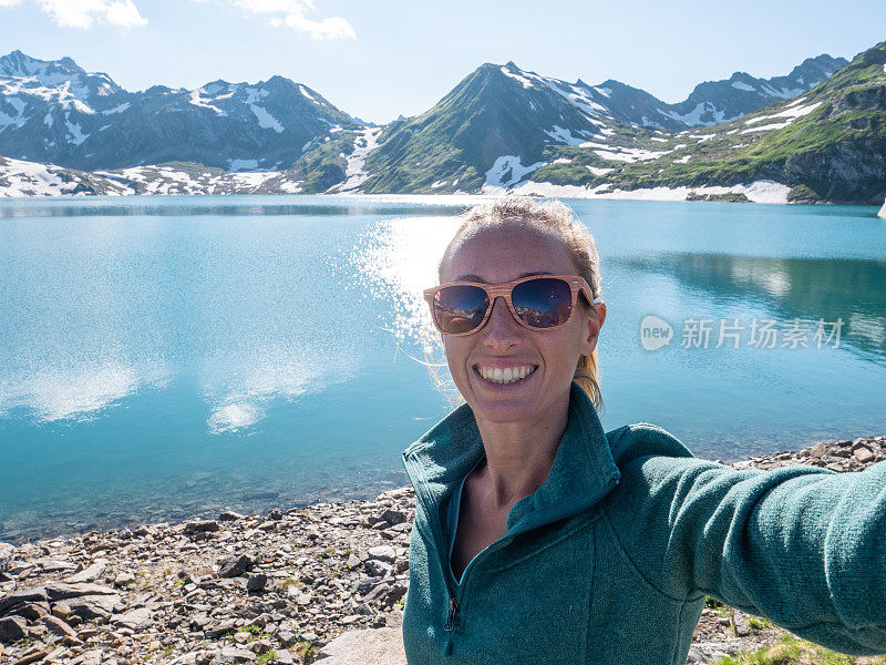 年轻女子在美丽的高山湖周围徒步旅行时自拍