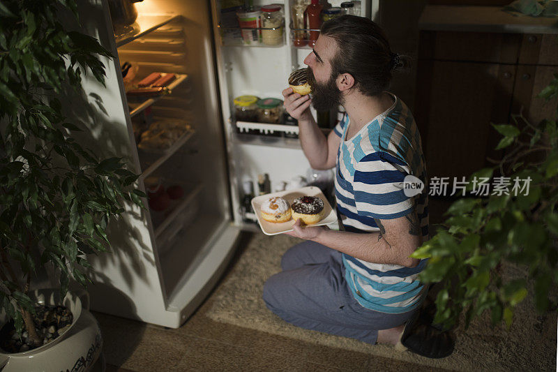 大胡子男人在冰箱前吃甜甜圈