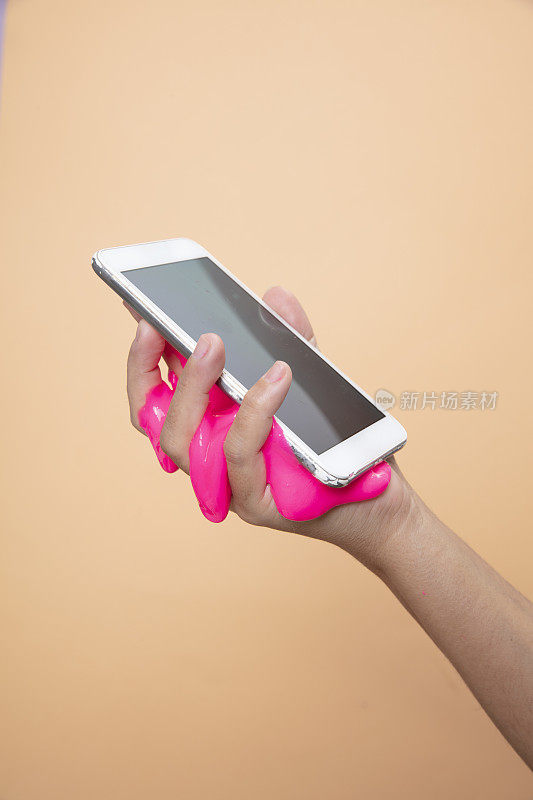 女人的手用智能手机与霓虹粉色黏液玩具在橙色波普艺术背景。