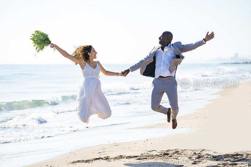 刚刚结婚度蜜月的新婚夫妇在海滩上跳高混合种族