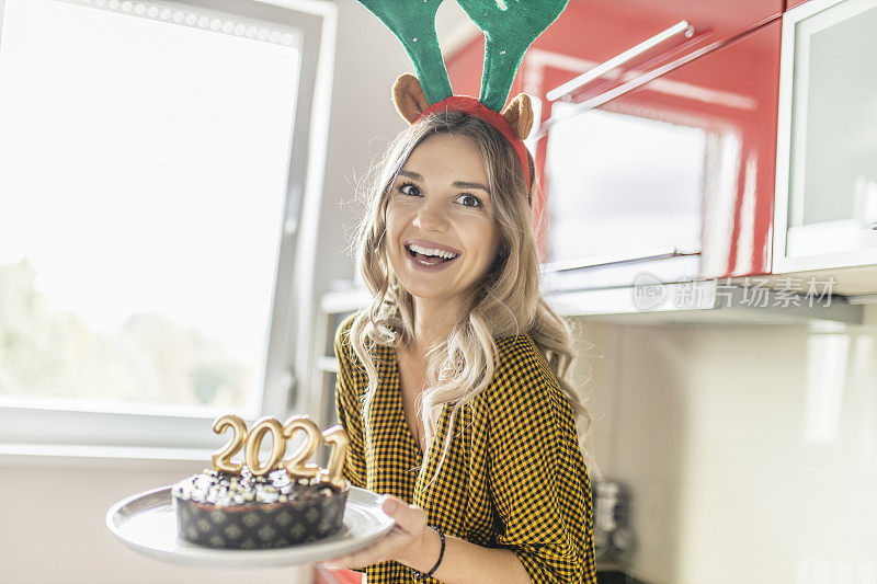 一名年轻女子正在制作并装饰巧克力蛋糕，蛋糕上点燃蜡烛，形状为2021年新年派对的数字