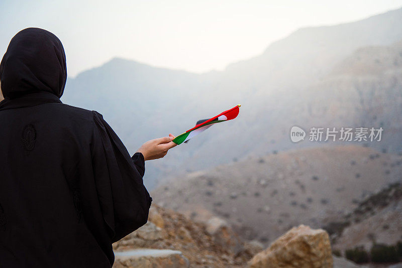 日落时分，一名阿联酋妇女在沙漠山区举着阿联酋国旗