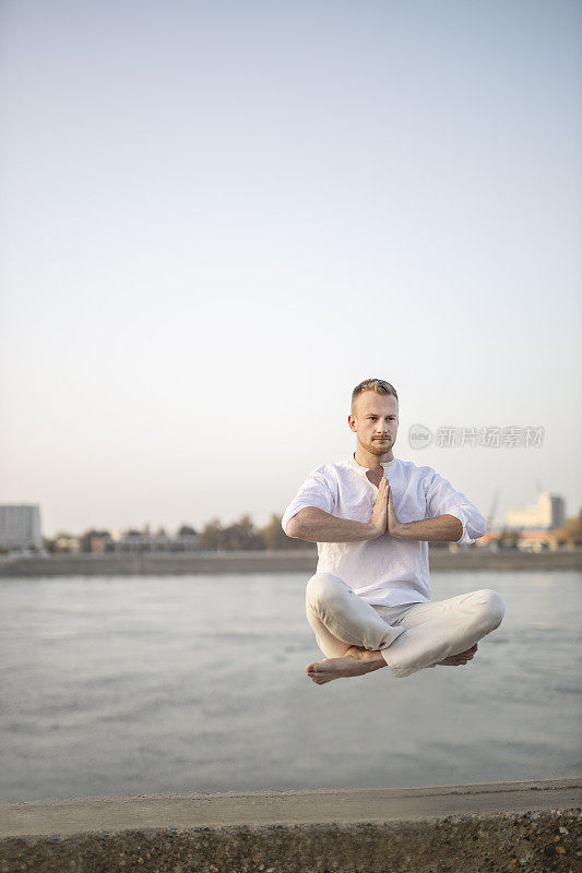 年轻美丽的男子在半空中沉思的肖像，漂浮在户外地面上，坐在莲花姿势，莲花身