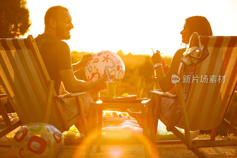 年轻的夫妇在甲板上享受夏日，鸡尾酒和充气