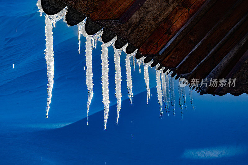 尖利的冰柱和融化的雪挂在屋顶的屋檐上