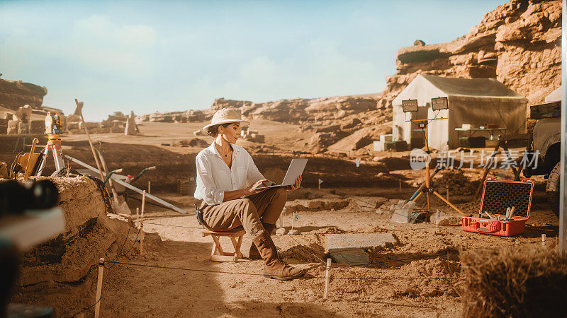 考古发掘遗址:有影响的女考古学家在做研究，用笔记本电脑分析附近出土的古代文明文化文物。著名历史学家的工作