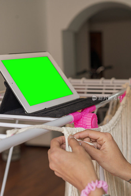 一个拉丁女人坐在沙发上，从平板电脑上学习虚拟的流苏课程，穿着舒适的衣服，在她的临时桌子上工作