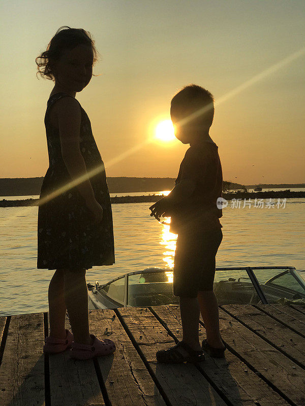 朋友，一个女孩和一个男孩，站在海湾的堤岸上欣赏夕阳。在夏日的傍晚散步。