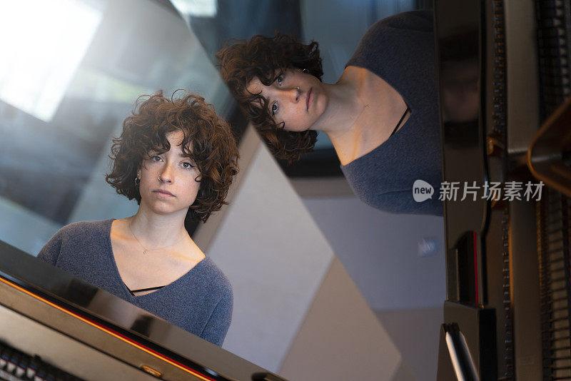 一头卷发的年轻女子坐在一架大钢琴前思考和弹奏