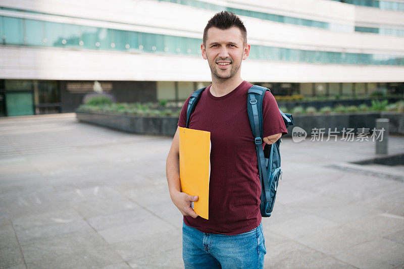 快乐的成年男学生站在大学前面