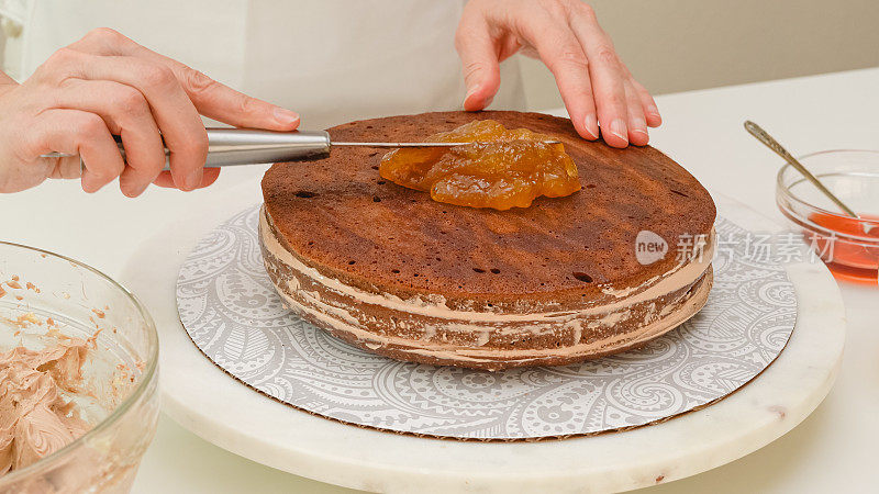 女人在蛋糕上涂杏酱。一步一步烘烤过程