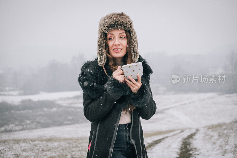 站在雪地上拿着一杯茶的年轻女子