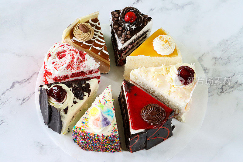 图像切片蛋糕品种的圆形防油羊皮纸，巧克力和樱桃蛋糕，黑森林蛋糕，红色天鹅绒，彩虹蛋糕，咖啡和大理石蛋糕，大理石效果的背景，重点在前景，高架视图