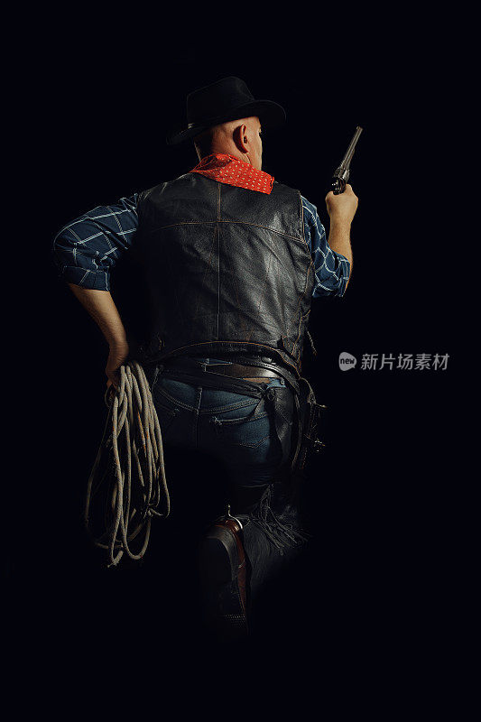 牛仔蹲着，握着绳子和枪的背影