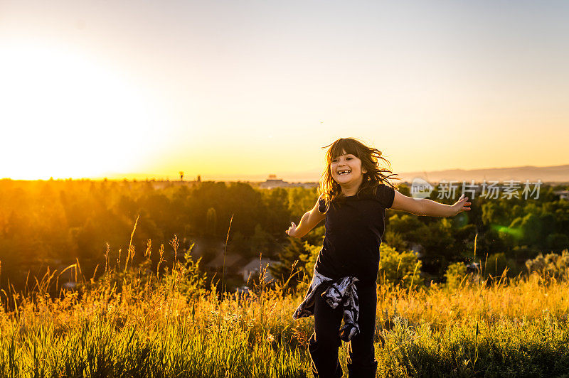 快乐的微笑的女孩嬉戏在夕阳下的荒野农村草地户外