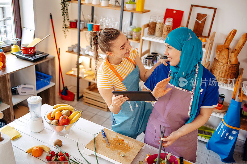 两名年轻女子正在用数码平板电脑寻找食谱，准备健康膳食