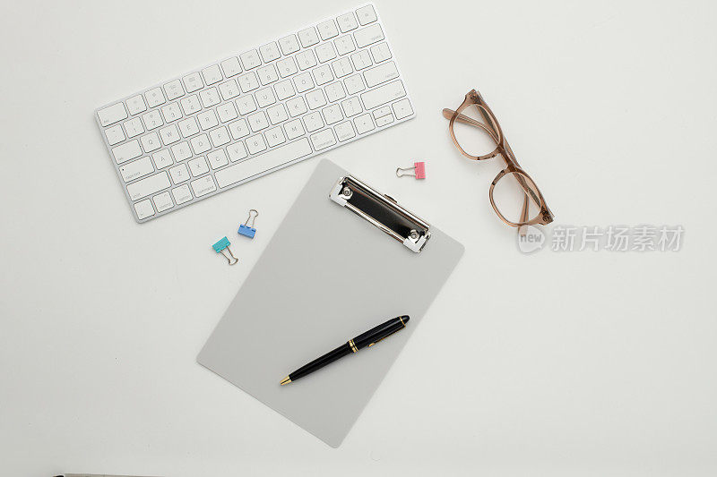 静物平面——灰色剪贴板、眼镜、键盘、夹子和一支笔