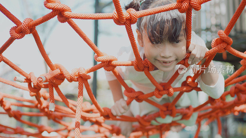小学混合亚洲女孩在蜘蛛网上玩得很开心，在学校操场上进行户外活动