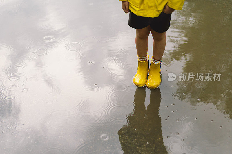 春天的一天，可爱的小男孩穿着雨衣和胶靴走过水坑