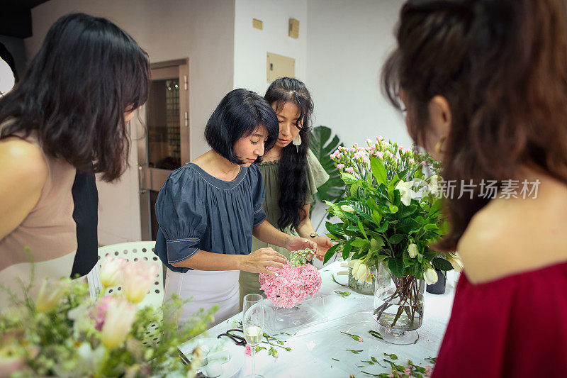 一位亚洲美丽的花艺女老师目前正在教花艺学生如何安排花艺材料，创造美丽的花艺作品。