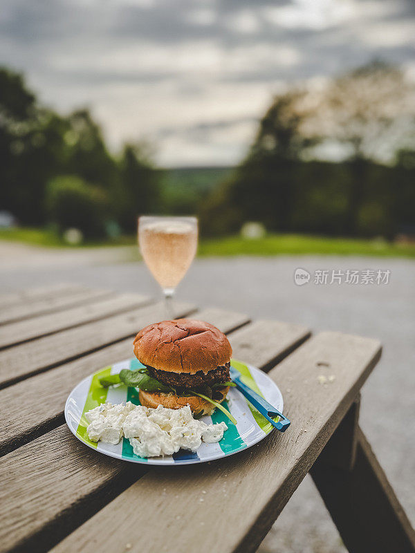 汉堡，土豆沙拉和一杯玫瑰红葡萄酒放在野餐桌上