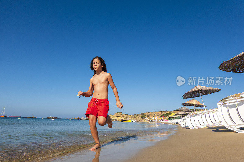 一个阳光明媚的早晨，一个英俊的12岁男孩在北爱琴海博斯卡达岛的海滩上慢跑。