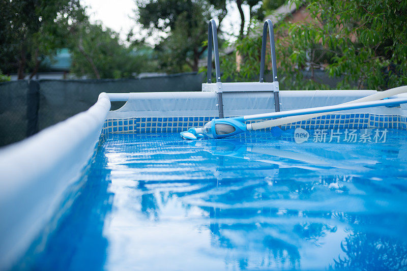 游泳池带真空吸尘器清洁工具。太阳能薄膜覆盖着游泳池。