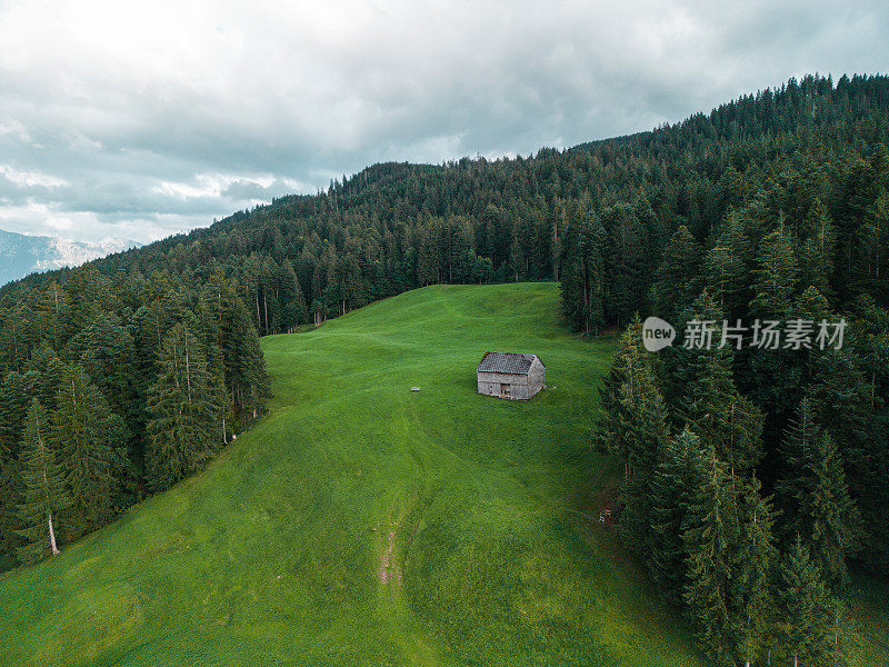 鸟瞰森林环绕的山间草地上的小屋