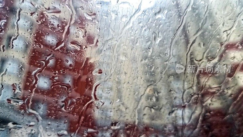 雨滴落在城市高层住宅楼的汽车挡风玻璃上的特写