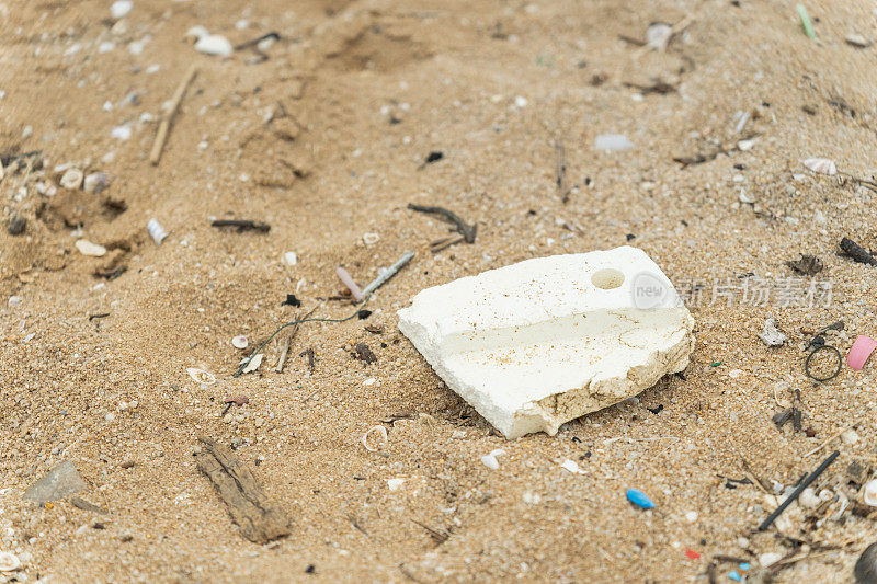 沙滩上破碎的塑料和泡沫材料的特写镜头，造成了沿海地区的环境污染问题。各种塑料碎片污染了该地区，导致废弃的旅游场所。