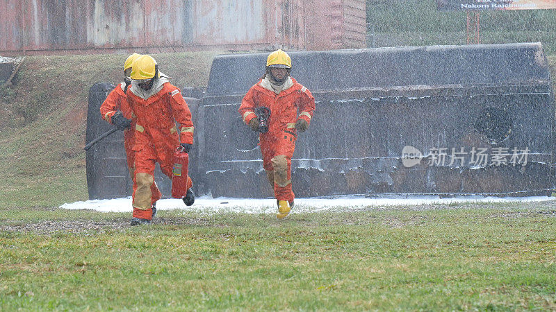 消防救援队员接受灭火器训练。消防队员使用消防水带与火焰进行化学水泡沫喷雾。消防队员戴安全帽，穿工作服