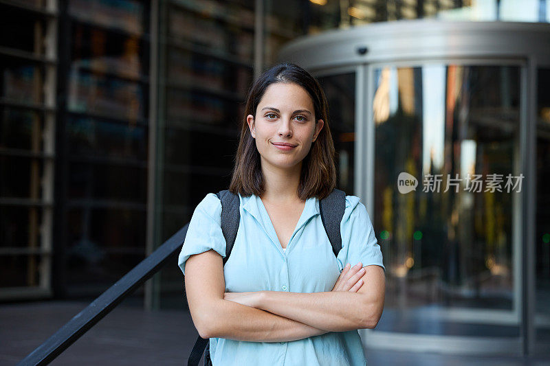 一个自信而成功的女商人双臂交叉站在办公楼外，展现出力量、独立和专业准备