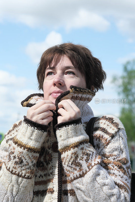 一个女人站在风飕飕的街上，把自己裹得严严实实