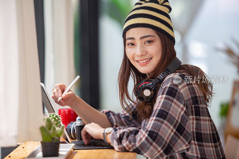 漂亮的亚洲女人在咖啡店工作与相机，平板电脑微笑着听音乐快乐。