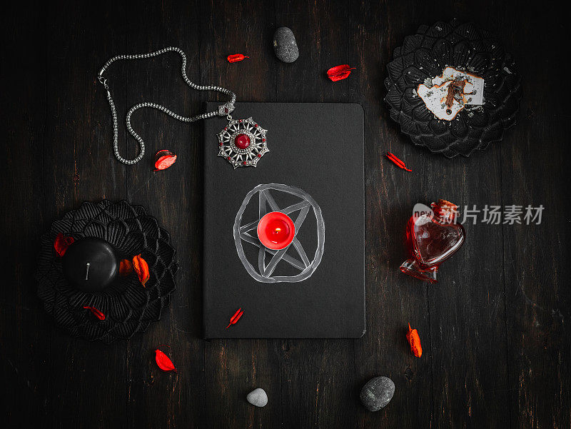 黑色皮革书与一个魔法标志，护身符，蜡烛，石头和红色药水在黑色的背景。
