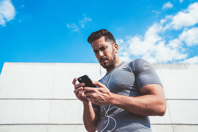 自信强壮的白人男性运动员在户外训练时检查智能手机健身应用程序结果的更新，保持体形，千禧一代运动员在博客上分享关于健康生活方式的出版物