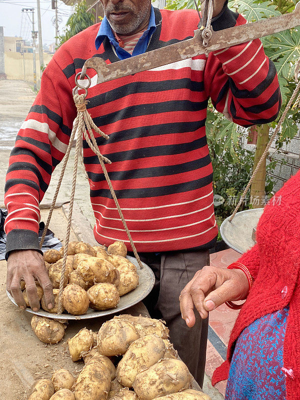 市场商贩在路边摊上卖土豆，在临时手推车摊上卖蔬菜，用天平称新鲜农产品，让面目全非的妇女购买，关注前景