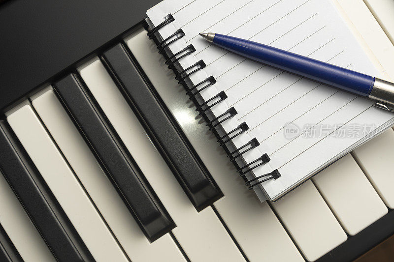 作曲概念:一个记事本和一支笔靠在钢琴的键盘上