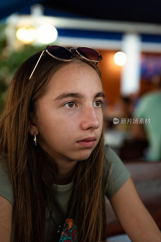 一个十几岁的女孩坐在日落时分的夏日户外餐厅的肖像