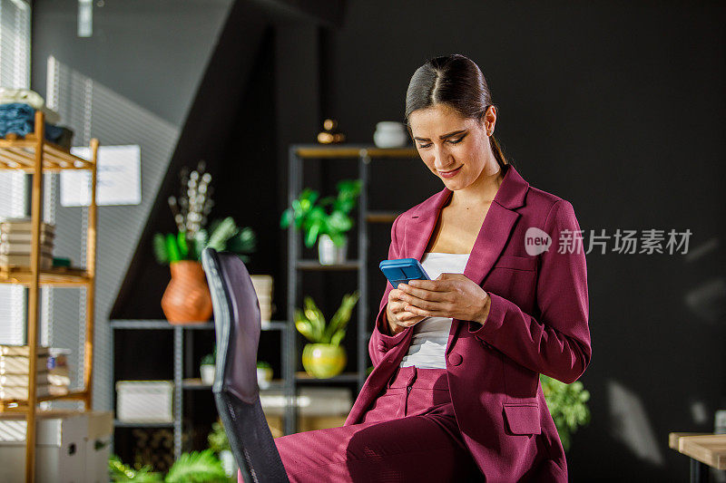 年轻的女商人坐在她的桌子边，通过智能手机回复短信