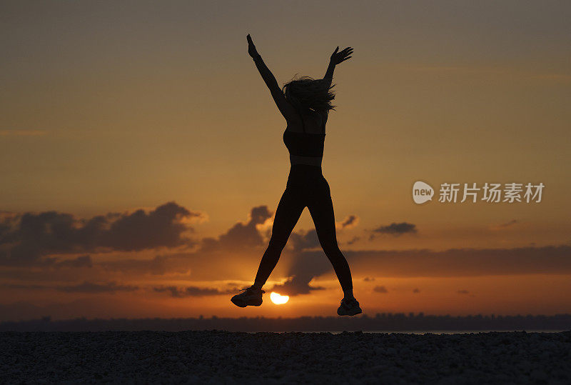 年轻美丽的女人在日出时在海滩上跳跃